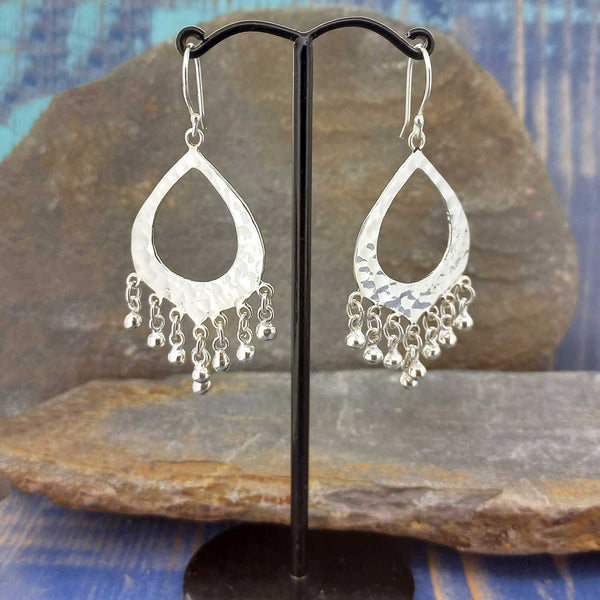 Silver teardrop Mexican earrings with dangling beads on a black stand against a stone background