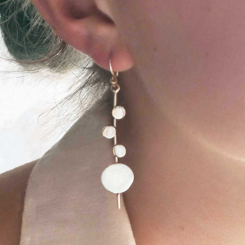 Close-up of a person wearing a dangling earring with circular spheres.