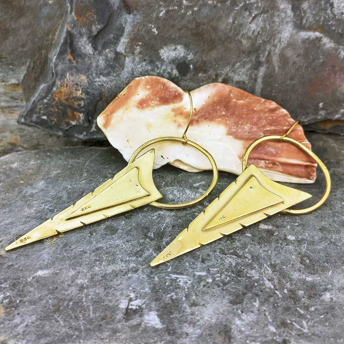 Gold geometric brass earrings on a stone surface with a shell in the background