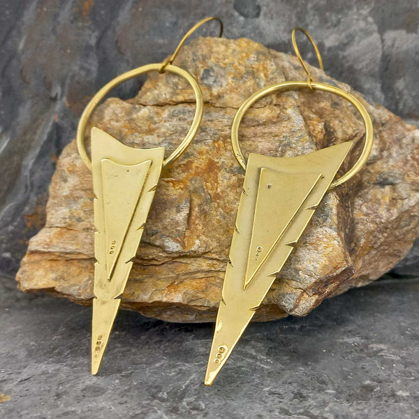 Gold coloured arrowhead-shaped brass earrings on a stone surface
