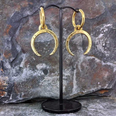 Gold hued brass crescent moon earrings on a black stand against a stone background