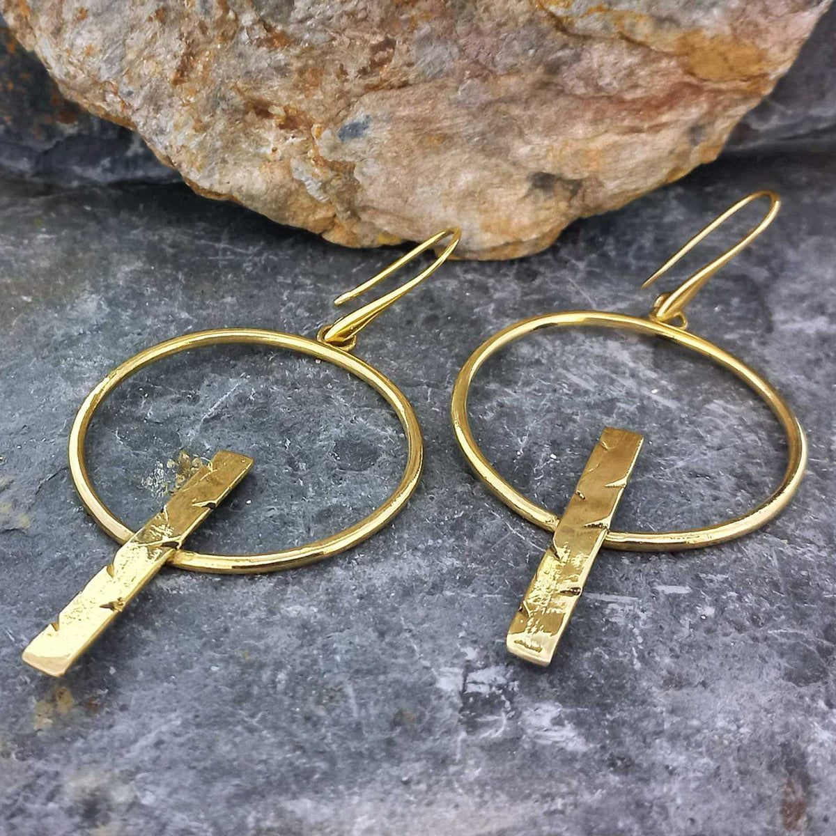 Gold hued brass unusual hoop earrings with vertical bars on a stone surface Main image
