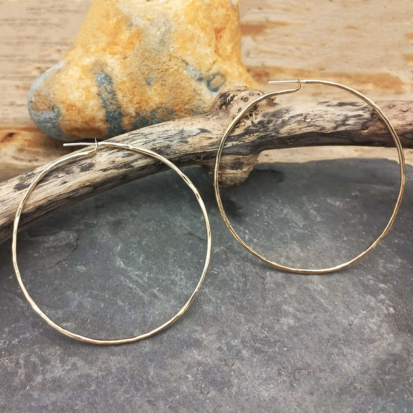 Gold hoop earrings on a stone surface with a rock in the background