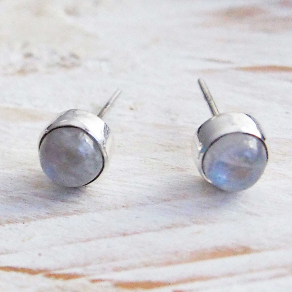 Pair of silver stud earrings with a light blue gemstone on a wooden surface