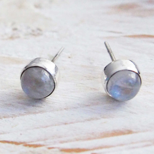 Pair of silver stud earrings with a light blue gemstone on a wooden surface