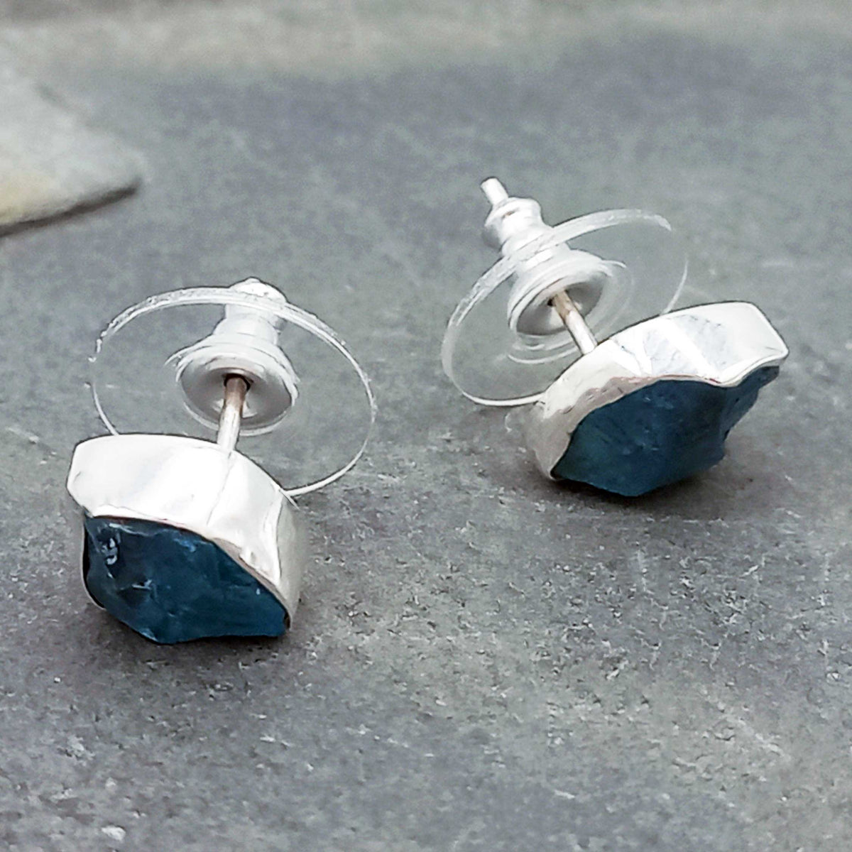 Silver and blue stud earrings on a gray stone surface