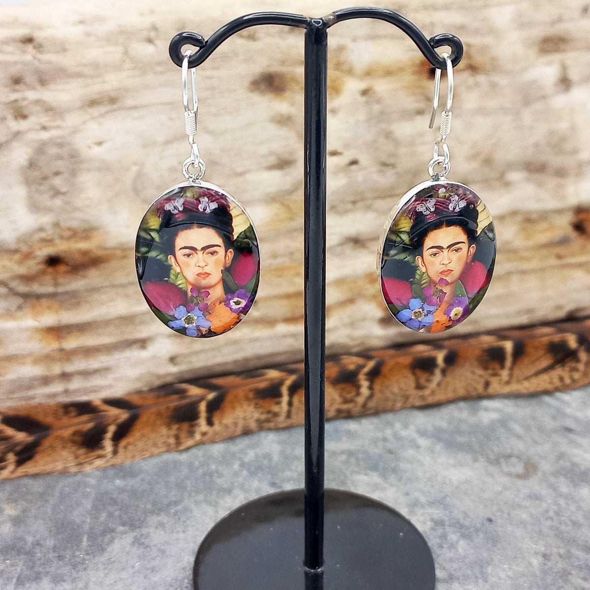 Frida Kahlo-themed earrings on a black stand with a wooden background