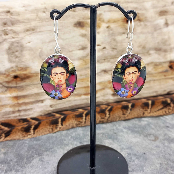 Frida Kahlo-themed earrings on a black stand with a wooden background