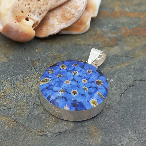Round blue floral pendant with silver frame on a stone surface