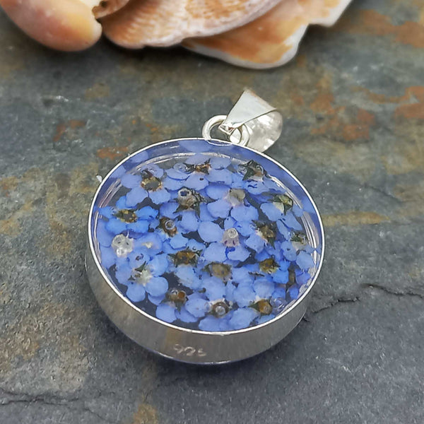 Back of Silver pendant with blue floral design on a stone surface