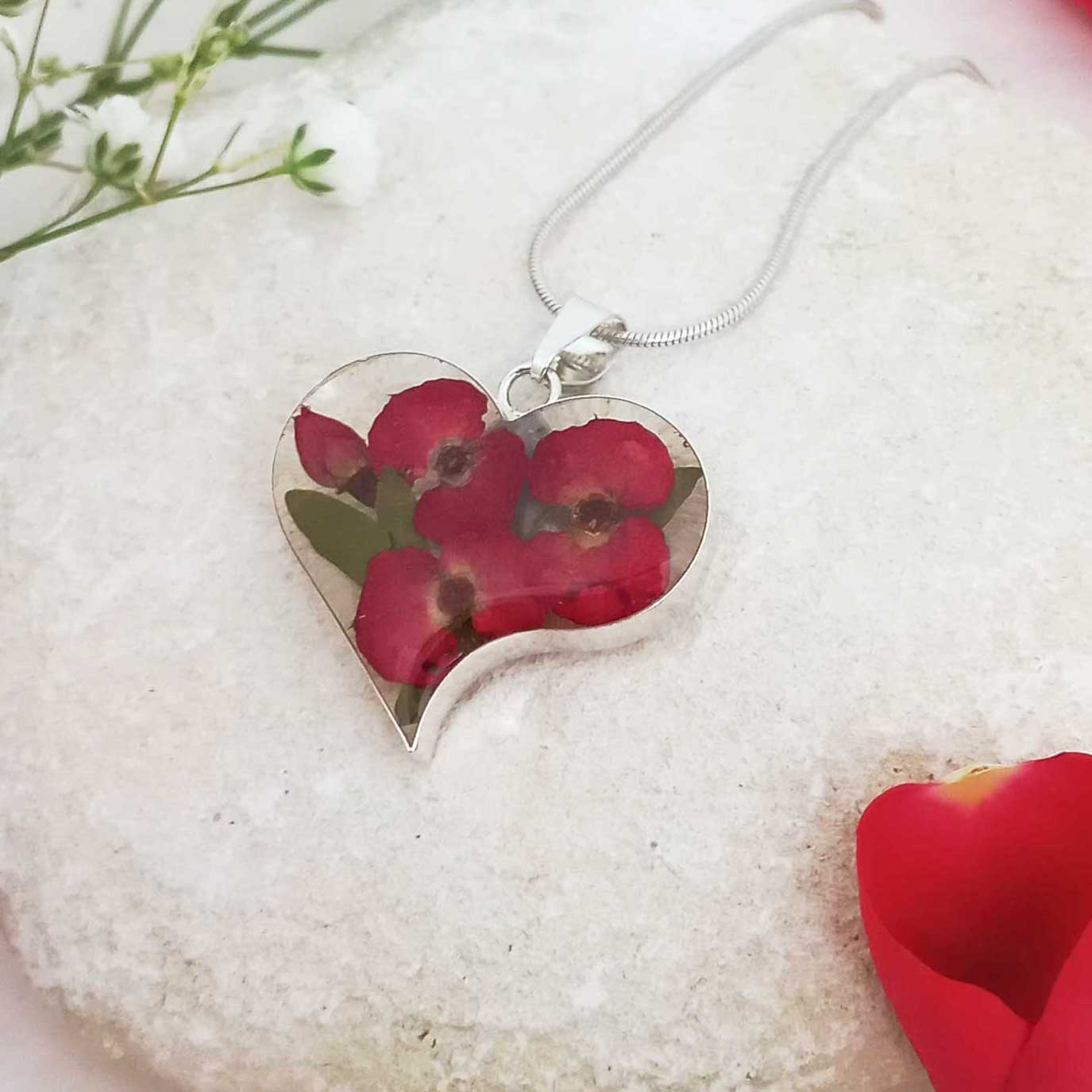 Heart-shaped silver pendant with real poppy flowers on a white stone surface
