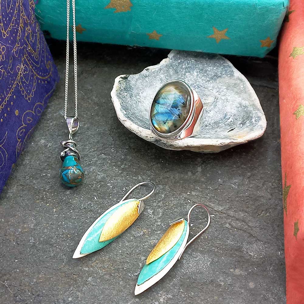 A collection of Mexican jewelry including a necklace with a blue pendant, and a pair of earrings displayed on a stone surface. Main image