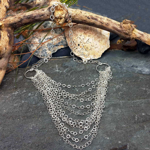 Silver chain necklace on a stone surface with a piece of driftwood.