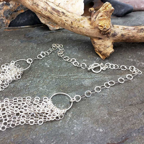 Silver chain necklace on a stone surface with driftwood in the background