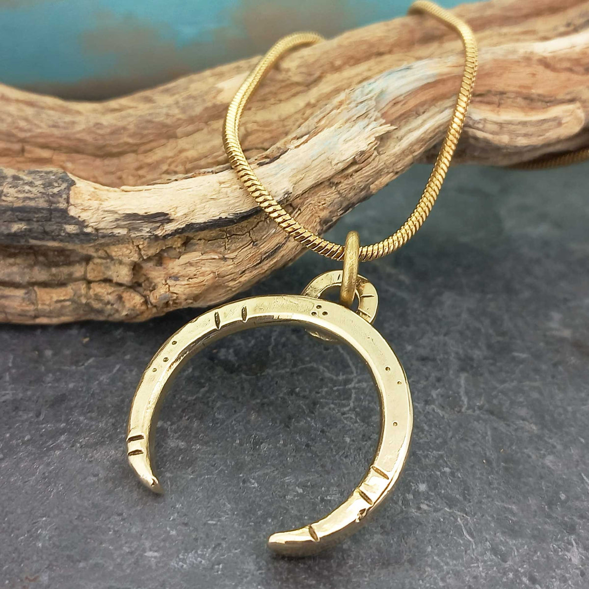 Gold crescent moon pendant on a gold-plated chain against a natural background
