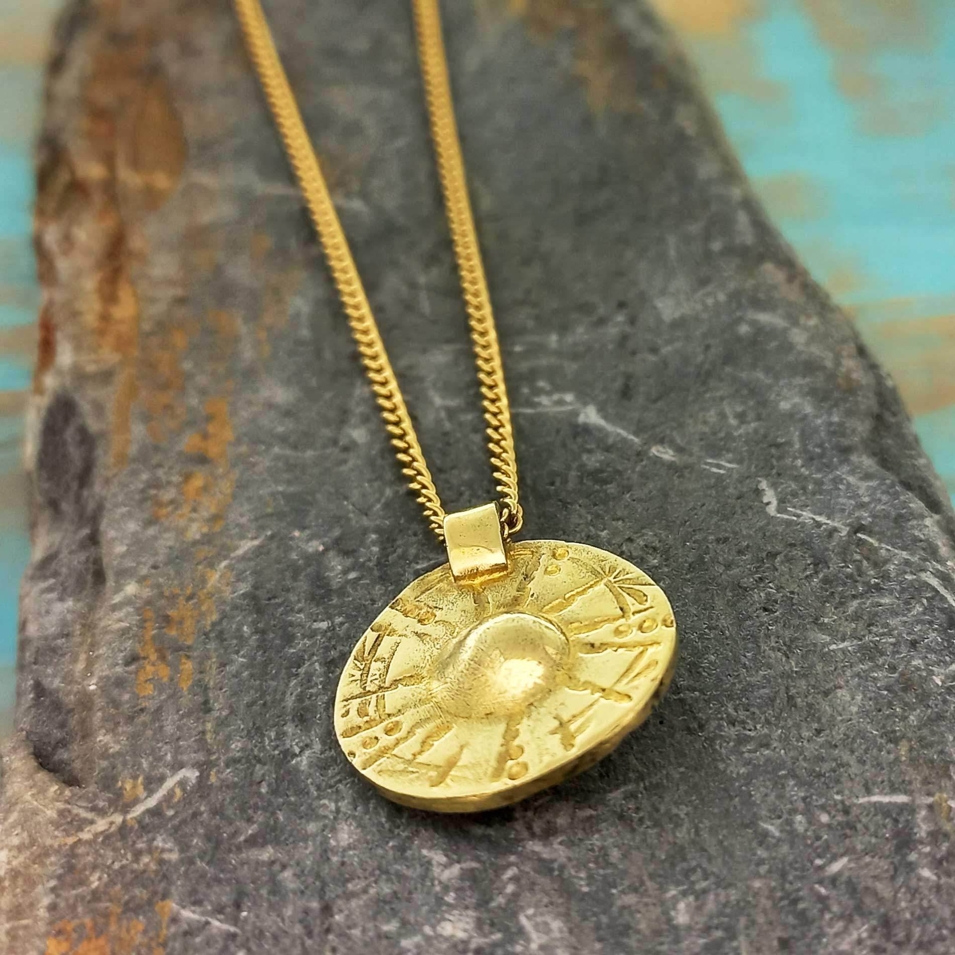 Gold coloured necklace with a round pendant on a textured stone surface