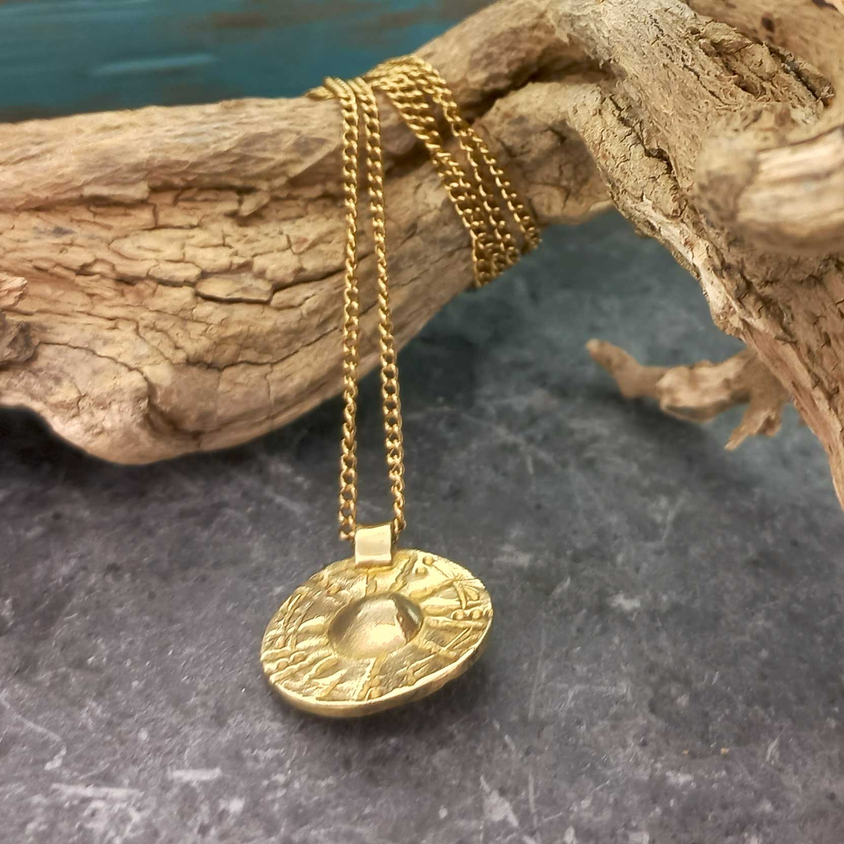 Gold hued brass necklace with a decorative pendant on a textured surface