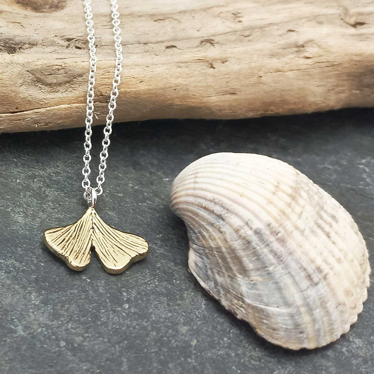 Gold leaf Ginkgo leaf necklace on a chain with a shell and wooden log in the background Main image