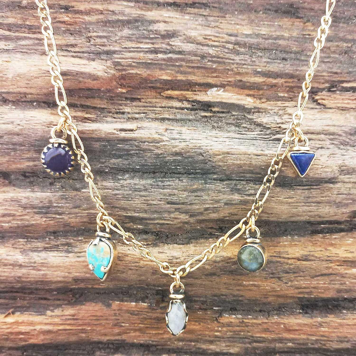 Gold coloured necklace with various gemstone pendants on a wooden surface