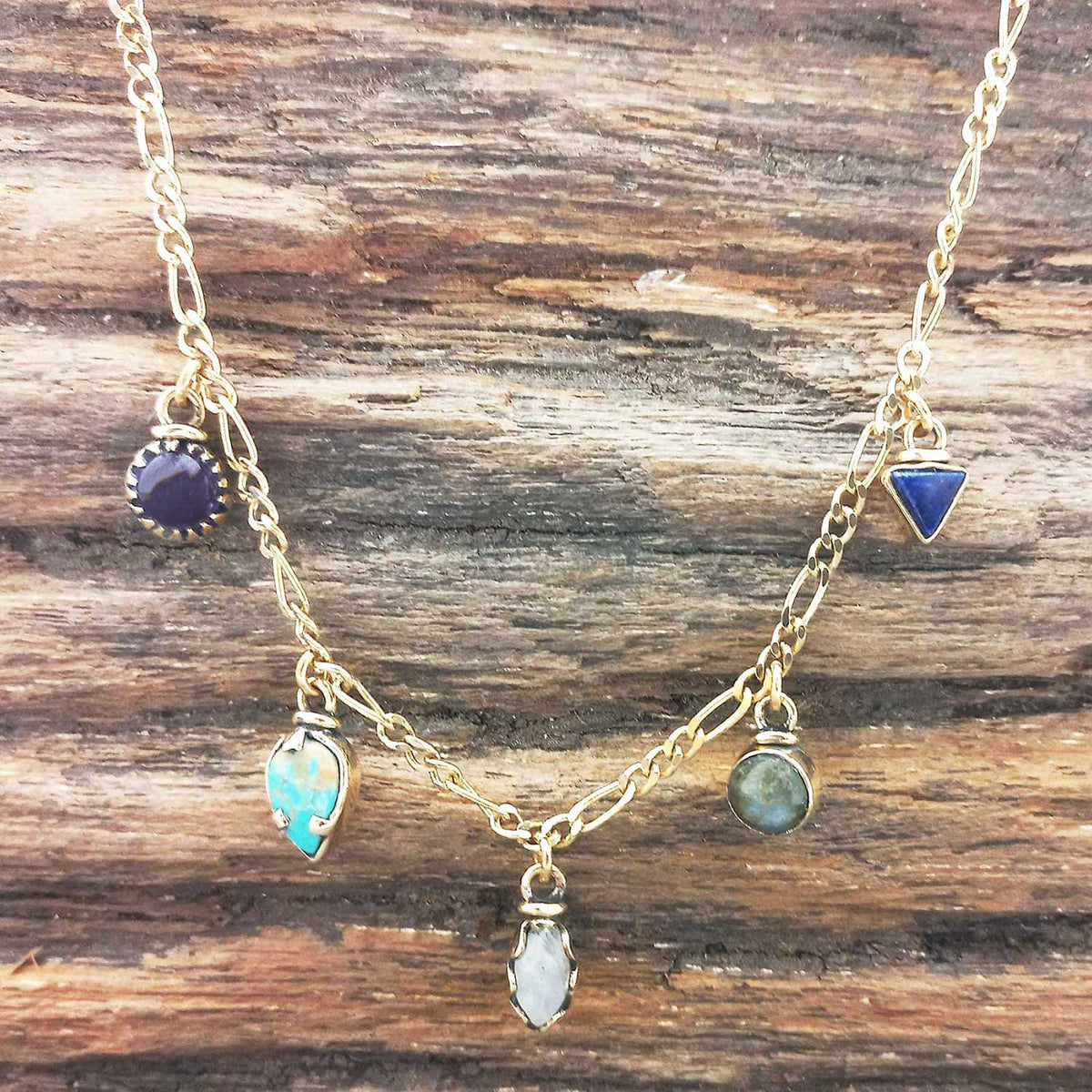 Gold coloured necklace with various gemstone pendants on a wooden surface