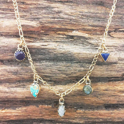 Gold coloured necklace with various gemstone pendants on a wooden surface