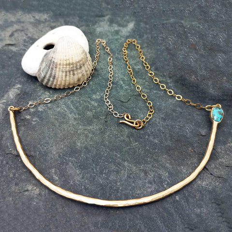 Unusual gold-tone necklace with a hammered curved bar, a delicate chain, and a small turquoise-blue stone.
