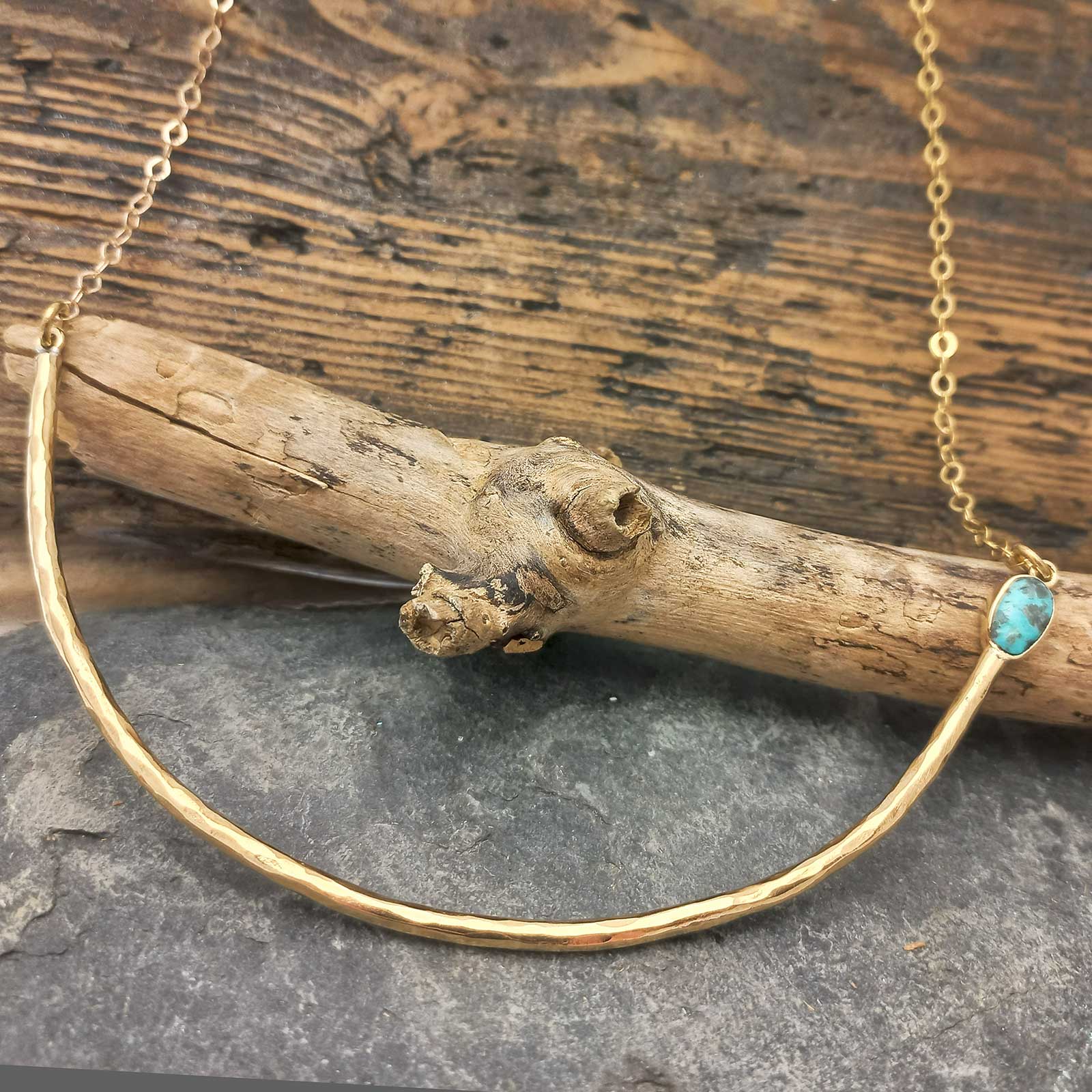 A gold-toned hammered half-circle brass necklace with a small turquoise stone accent.