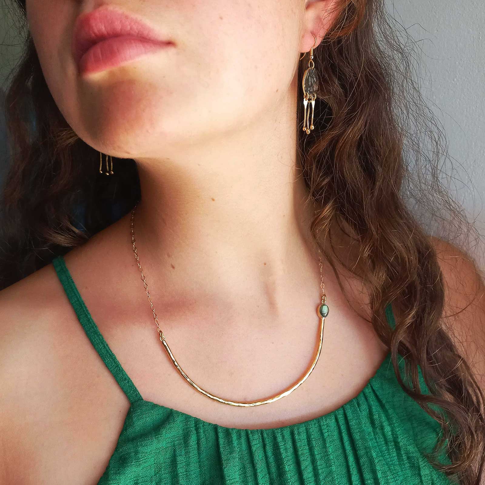 A close-up lifestyle shot of a woman wearing an unusual delicate gold crescent-shaped brass necklace with a Labradorite stone.