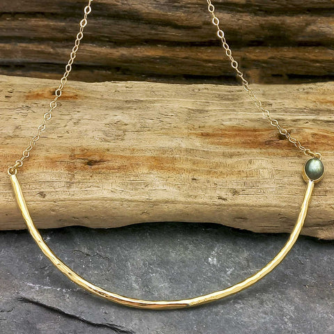 A handmade gold brass necklace with a hammered curved bar and a green Labradorite gemstone, suspended from a brass chain.