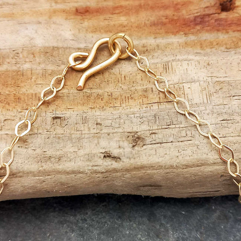 Close-up of a brass chain necklace clasp resting on a textured piece of wood, with the chain extending toward both sides.