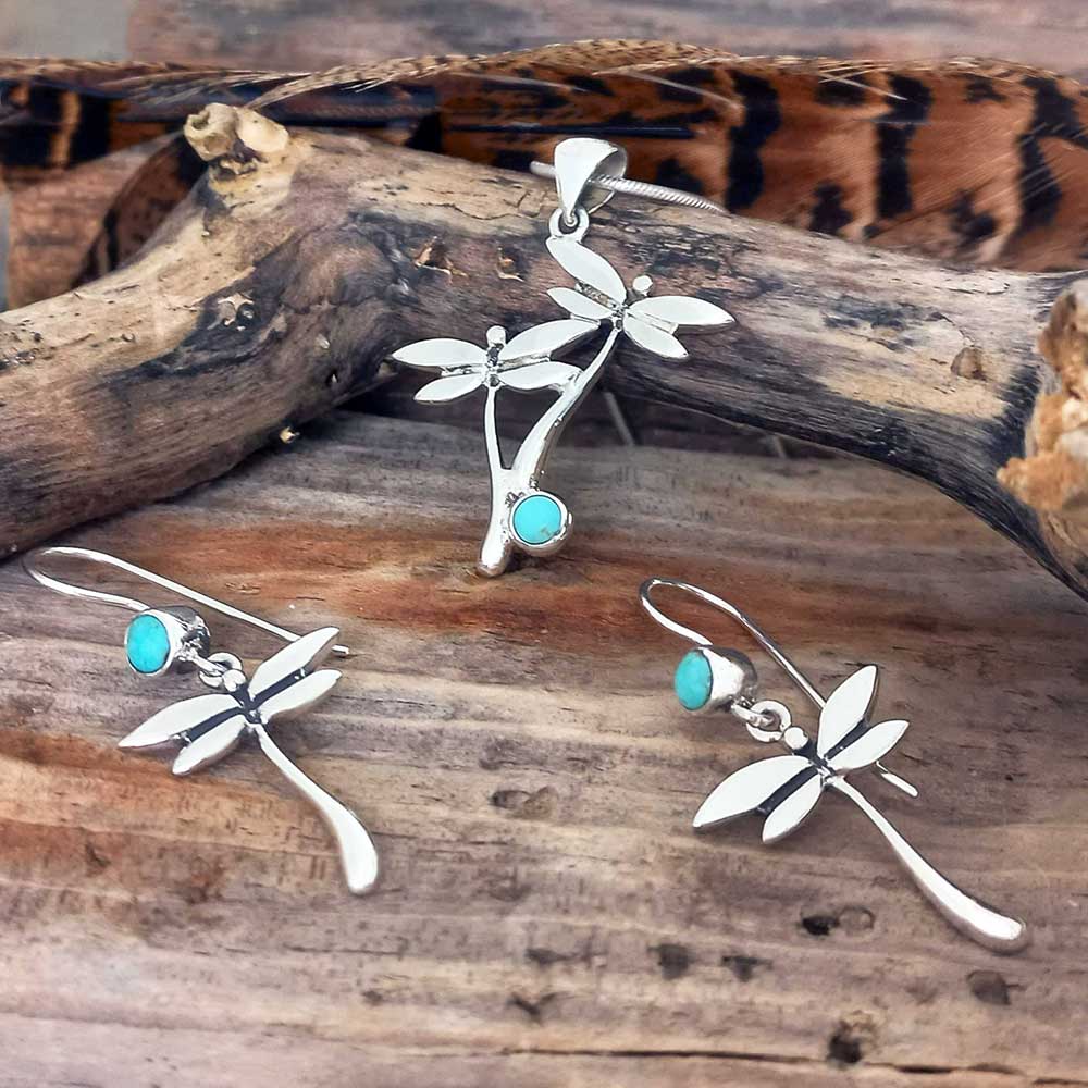 Silver jewellery pendants earring set with Turquoise stone dragonfly designs on a wooden surface.