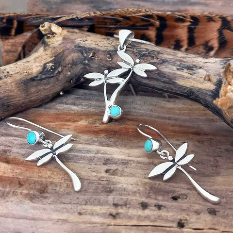 Silver jewellery pendants earring set with Turquoise stone dragonfly designs on a wooden surface.