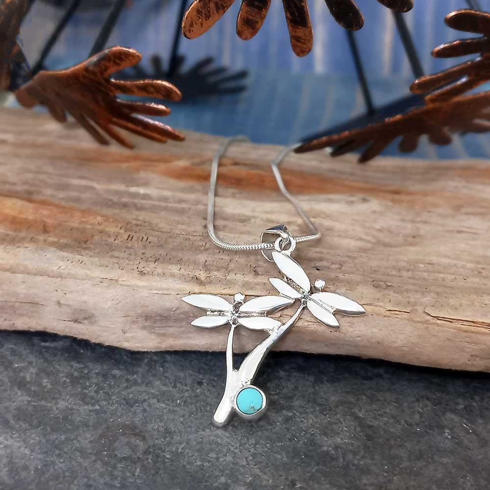Silver necklace with a dragonfly pendant and turquoise stone on a wooden surface