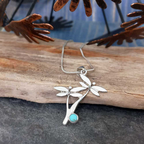 Silver necklace with a dragonfly pendant and turquoise stone on a wooden surface