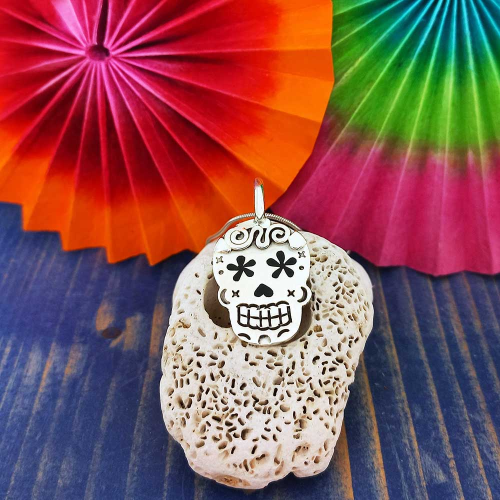 Decorative stone with a skull pendant on a blue surface with colorful paper fans in the background