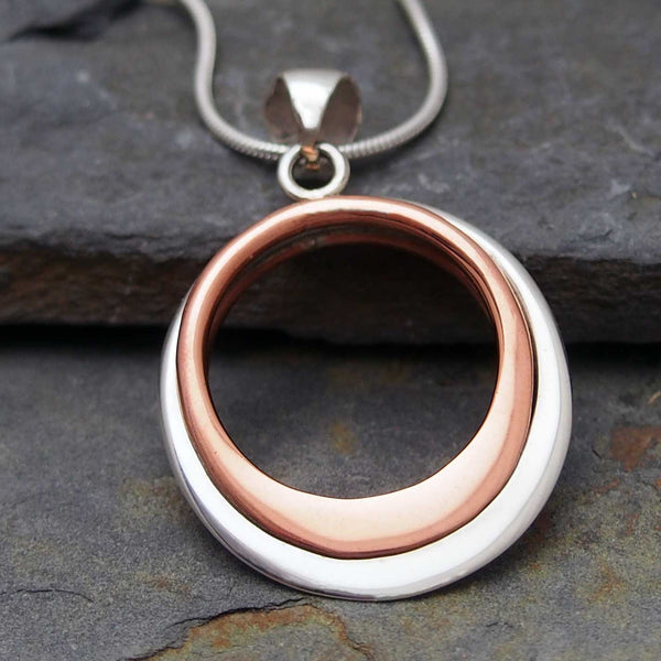 Necklace with a circular pendant featuring two rings, one copper and one silver, on a stone surface.