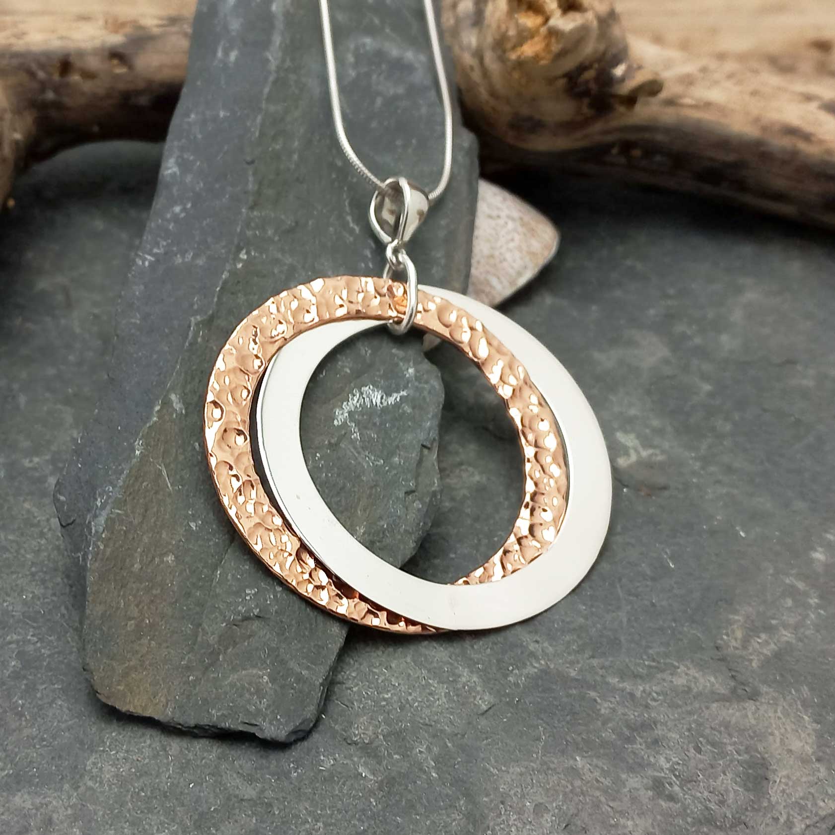 Two-toned circular pendant on a dark stone surface with wooden elements in the background