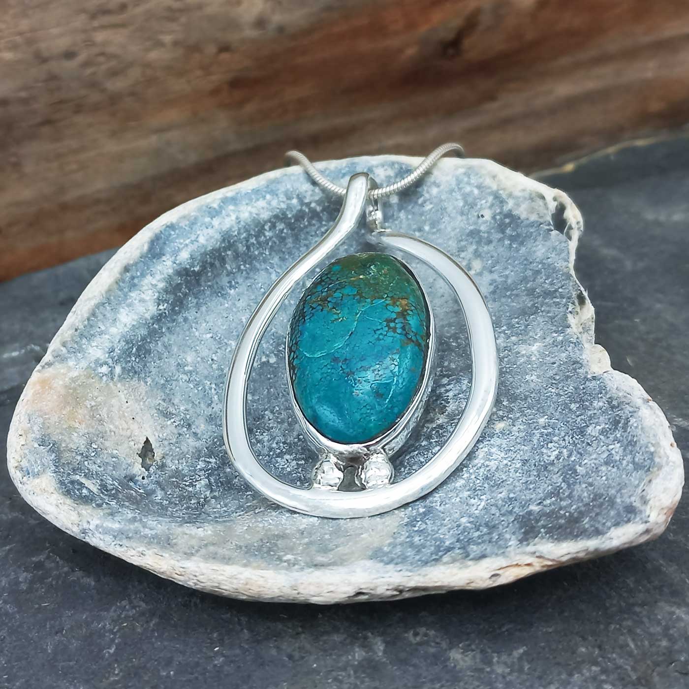 Chrysocolla green blue stone pendant in a silver setting on a rock