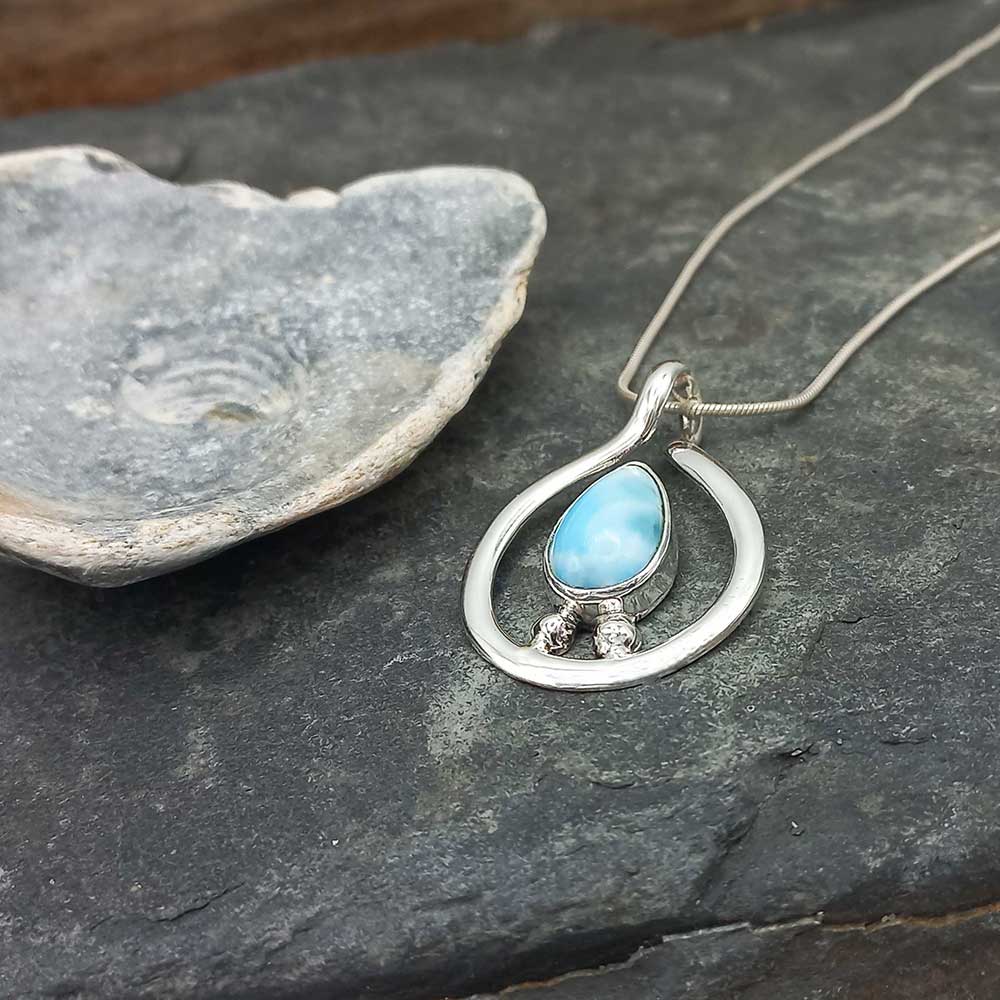 Silver pendant with a Larimar stone on a dark stone surface