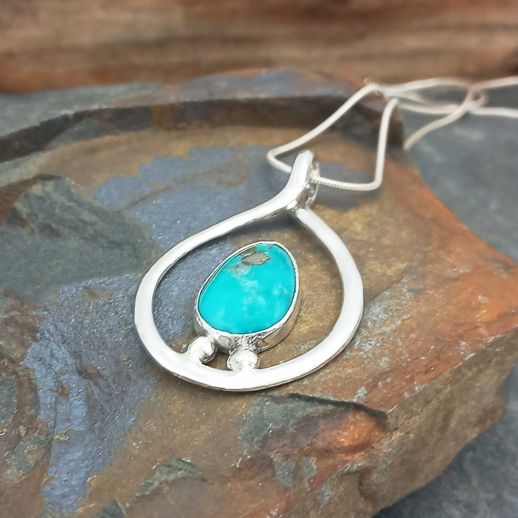 Silver pendant with a turquoise stone on a stone surface