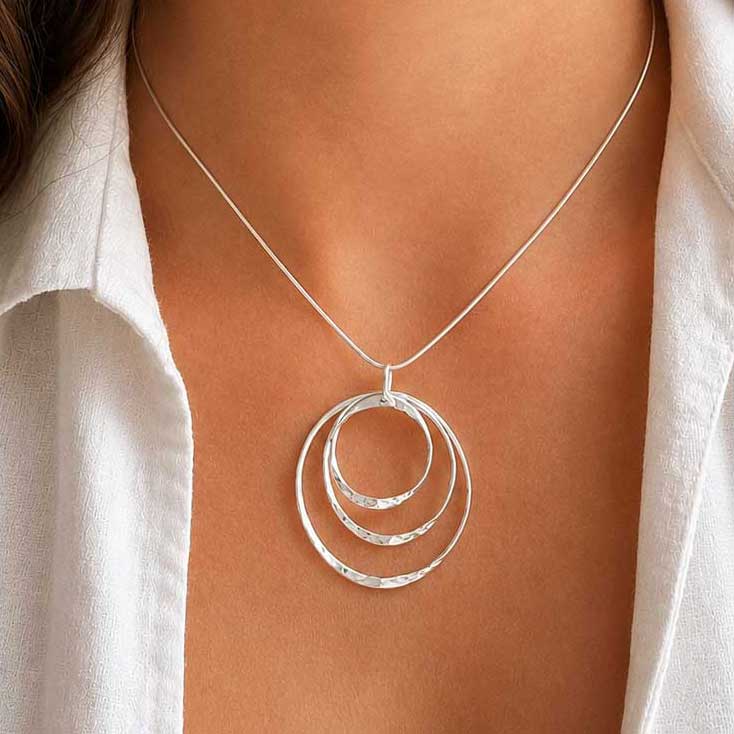 A sterling silver necklace with three textured concentric rings worn on a model's neck, styled with a white collared shirt.
