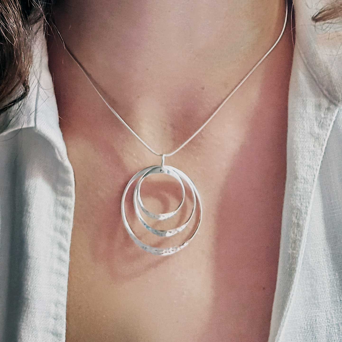 Silver necklace with a circular pendant on a person wearing a white shirt.