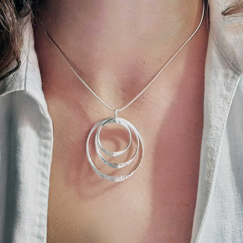 Silver necklace with a circular pendant on a person wearing a white shirt.