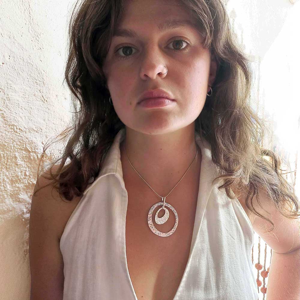 Woman wearing a silver necklace with a circular pendant against a neutral background