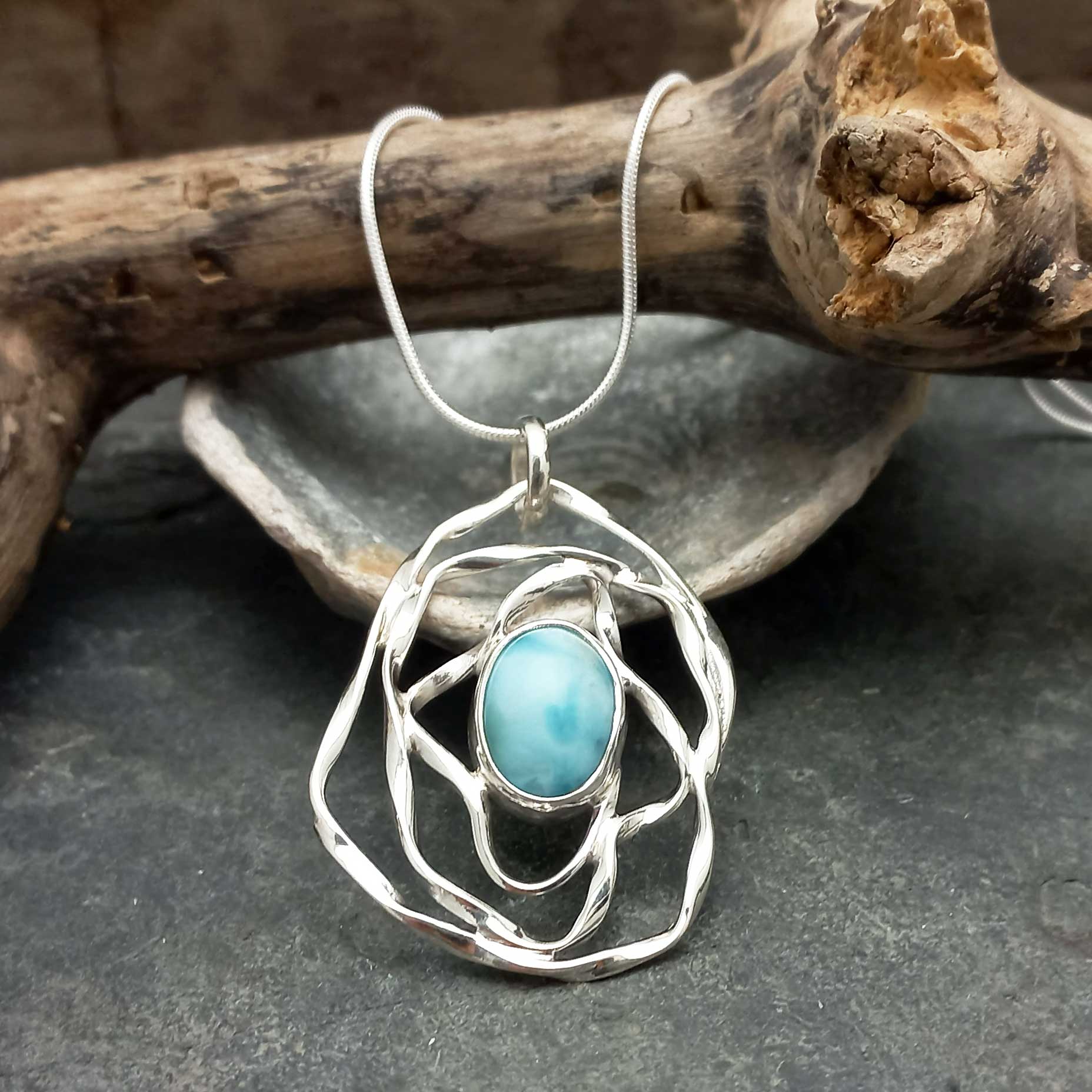 Silver pendant with a turquoise Larimar stone on a dark surface with wooden elements in the background