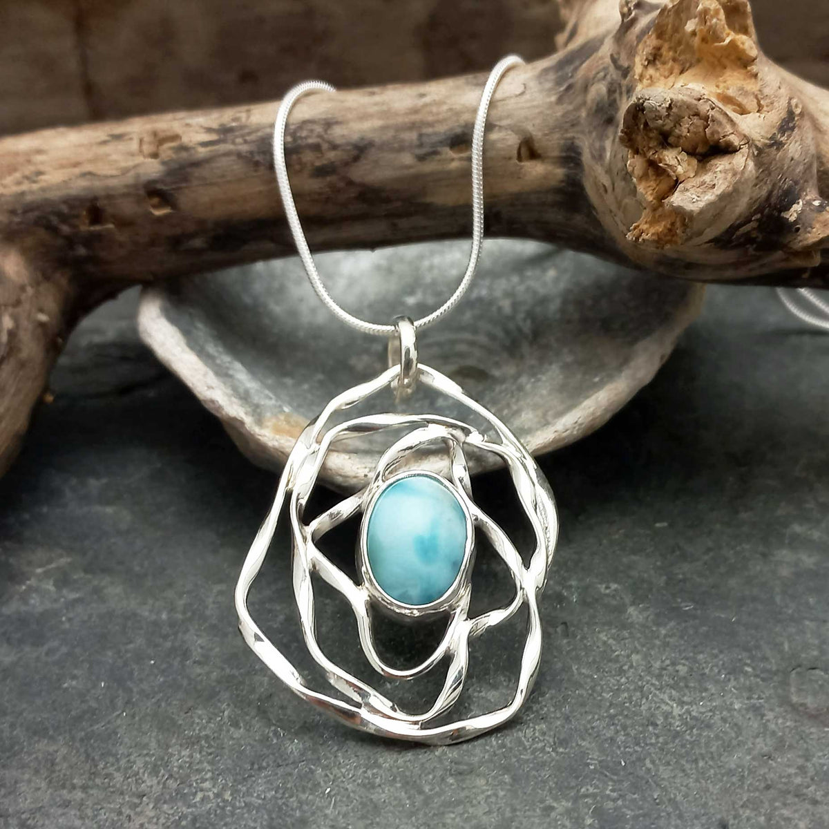 Silver pendant with a turquoise Larimar stone on a dark surface with wooden elements in the background