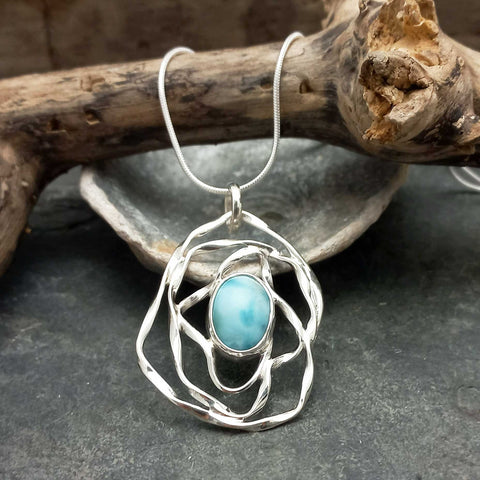 Silver pendant with a turquoise Larimar stone on a dark surface with wooden elements in the background