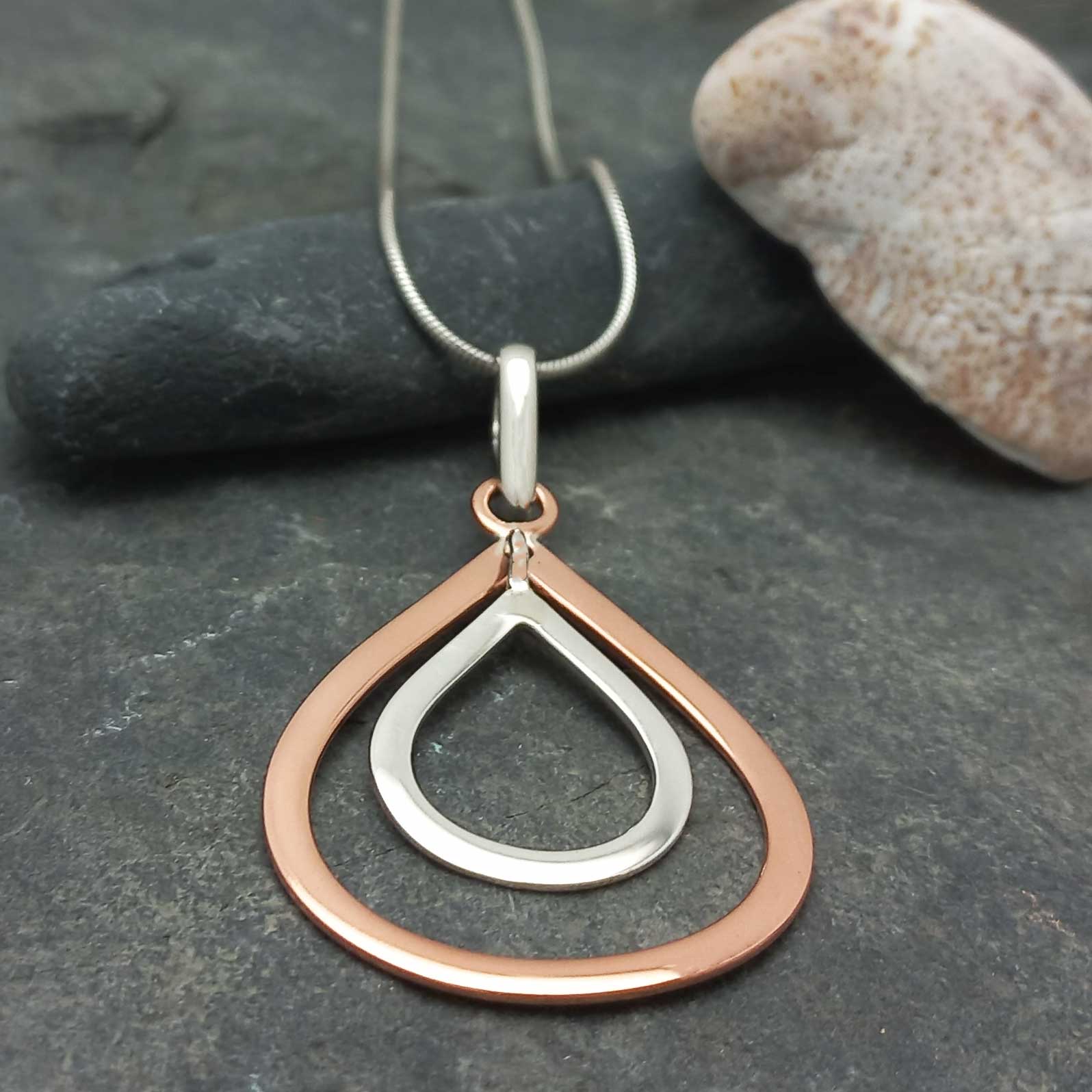 Two-toned silver copper teardrop necklace on a dark stone surface