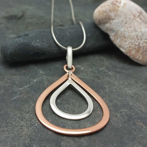 Two-toned silver copper teardrop necklace on a dark stone surface
