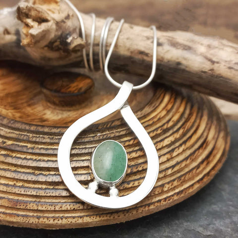 Sterling silver pendant with a green aventurine stone on a wooden surface.